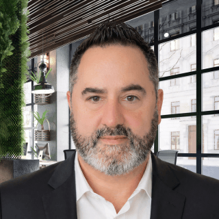 Professional man with a salt-and-pepper beard wearing a black blazer in a modern office.